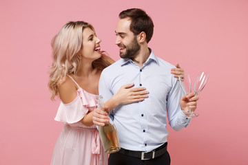 Funny young couple two guy girl in party outfit celebrating posing isolated on pastel pink background. Valentine's Day Women's Day birthday holiday party concept. Holding glass bottle of champagne.