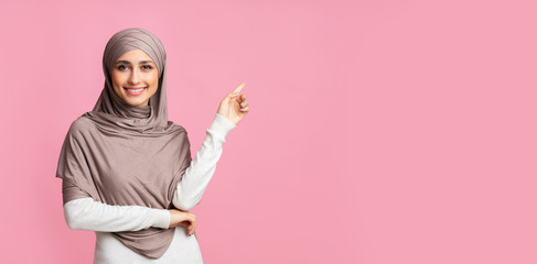 Smiling arabian girl pointing at copy space over pink background