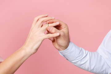 Close up cropped photo of female and male hold, putting proposal ring on finger isolated on pink...