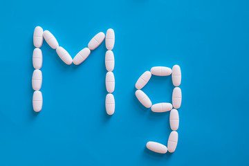 Magnesium tablets in a shape of Mg element on blue background