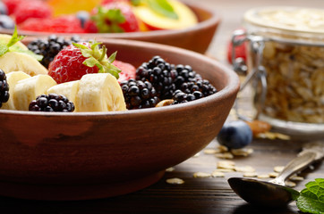 Fruit healthy muesli with banana strawberry almonds and blackberry in clay dish on wooden kitchen table