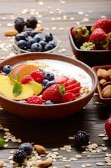 Fruit healthy muesli with peaches strawberry almonds and blackberry in clay dish with yogurt on wooden kitchen table