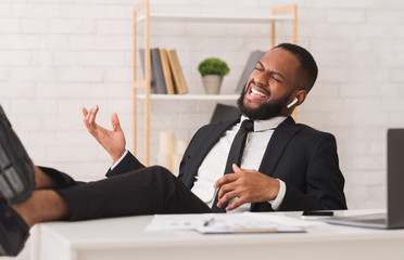 Emotional afro businessman listening to music at workplace