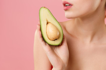 Close up cropped half naked woman 20s perfect skin nude make up hold in hand fresh ripe avocado isolated on pastel pink background studio portrait. Skin care healthcare cosmetic procedures concept.