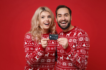 Merry young couple guy girl in Christmas knitted sweaters posing isolated on bright red background....