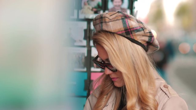 A young Parisian chooses a postcard in a street shop. Attractive girl in beret and sunglasses buys a card for memory of the journey.