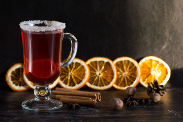 Glass cup with sugar on top of mulled wine, spices and pieces of oranges on the black background