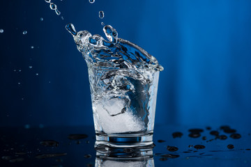 a piece of ice and a splash fall into a glass of water or vodka, all under water in a round vase