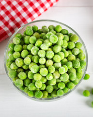 Frozen green peas in bowl on wooden background. Selective focus.