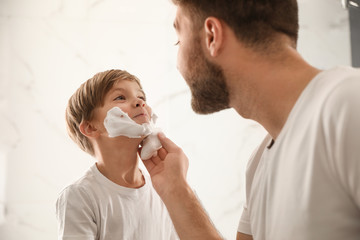 Dad applying shaving foam onto son's face in bathroom