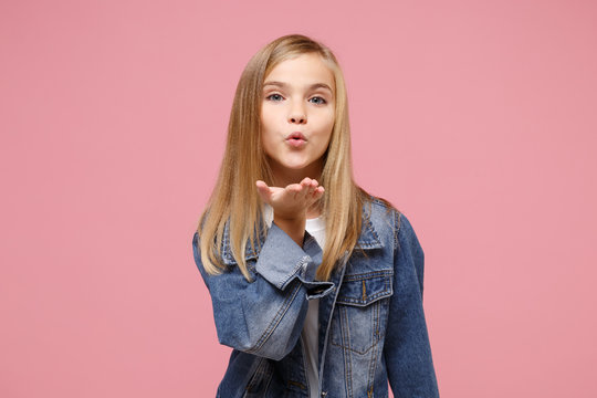 Pretty little blonde kid girl 12 13 years old in denim jacket isolated on pastel pink background children studio portrait. Childhood lifestyle concept. Mock up copy space. Blowing sending air kiss. St...