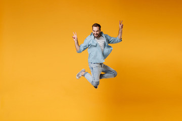 Fototapeta na wymiar Smiling young bearded man in casual blue shirt posing isolated on yellow orange background studio portrait. People sincere emotions lifestyle concept. Mock up copy space. Jumping showing victory sign.