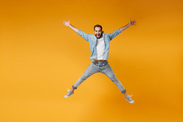 Fototapeta na wymiar Joyful young bearded man in casual blue shirt posing isolated on yellow orange wall background studio portrait. People emotions lifestyle concept. Mock up copy space. Jumping, spreading hands, legs.