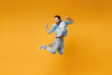Fototapeta na wymiar Happy young bearded man in casual blue shirt posing isolated on yellow orange background, studio portrait. People sincere emotions lifestyle concept. Mock up copy space. Jumping doing winner gesture.
