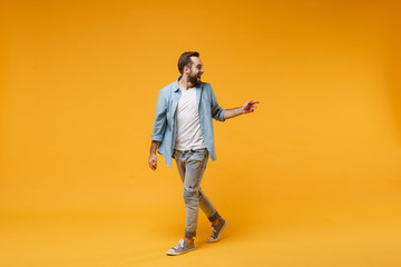 Fototapeta na wymiar Excited young bearded man in casual blue shirt posing isolated on yellow orange background studio portrait. People emotions lifestyle concept. Mock up copy space. Looking, pointing index finger aside.