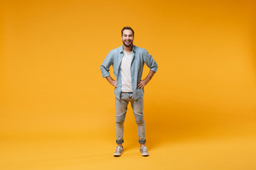 Fototapeta na wymiar Cheerful young bearded man in casual blue shirt posing isolated on yellow orange background, studio portrait. People emotions lifestyle concept. Mock up copy space. Standing with arms akimbo on waist.