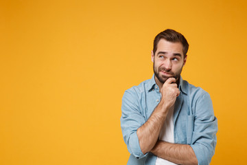 Pensive young bearded man in casual blue shirt posing isolated on yellow orange background studio...