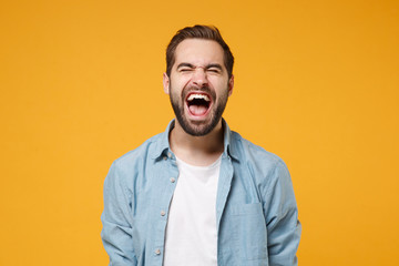 Crazy young bearded man in casual blue shirt posing isolated on yellow orange background studio...