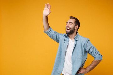 Cheerful young bearded man in casual blue shirt posing isolated on yellow orange background in...