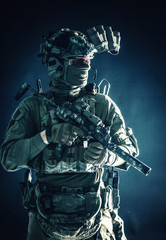 Anti-terrorist squad fighter, army elite forces soldier in combat uniform and tactical ammunition, armed mini submachine gun, wearing night-vision device, low key studio portrait on black background