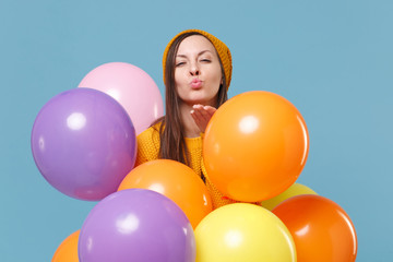Fototapeta na wymiar Young woman girl in sweater hat posing isolated on blue background. Birthday holiday party, people emotion concept. Mock up copy space. Celebrating hold colorful air balloons blowing sending air kiss.