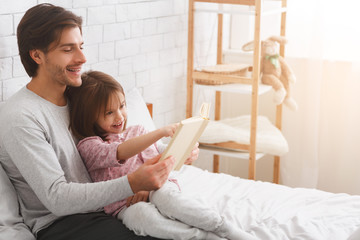 Little daughter and father enjoying book, spending weekend together