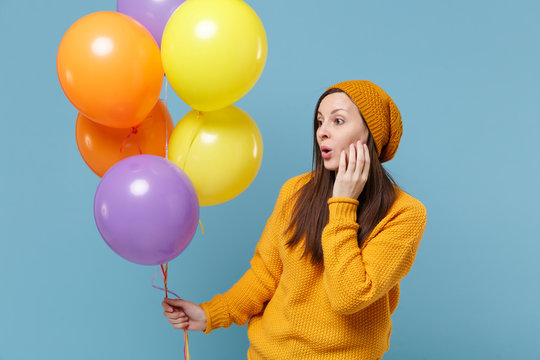 Amazed young woman girl in sweater and hat posing isolated on blue background. Birthday holiday party people emotions concept. Mock up copy space. Celebrating hold colorful air balloons looking aside.
