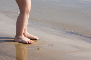 Child feet barefoot on the sand beach near water