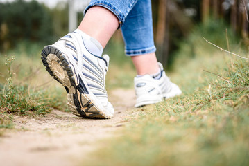 Woman's legs going on field or forest in white sneakers.
