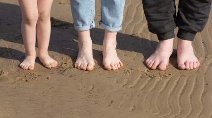 Fototapeta na wymiar Child feet, woman feet and man feet barefoot standing in a row on the sand beach