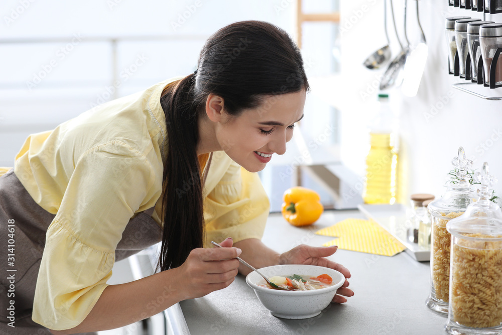 Wall mural young woman eating tasty vegetable soup at countertop in kitchen