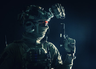 Side view portrait of army soldier, modern combatant, special forces fighter in helmet, night-vision device, radio headset, hiding identity behind mask, armed service pistol, low key studio shoot