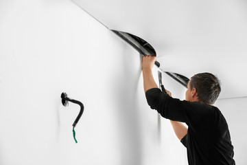 Repairman installing white stretch ceiling in room