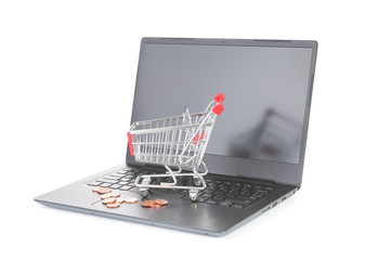 Shopping trolley and coins on laptop on white background