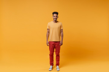 Smiling young african american guy in casual clothes posing isolated on yellow orange wall background, studio portrait. People sincere emotions lifestyle concept. Mock up copy space. Looking camera. - obrazy, fototapety, plakaty