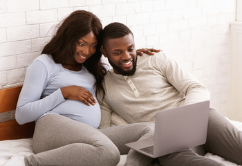 Happy pregnant couple choosing furniture for baby room online