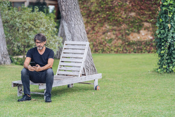Fototapeta premium attractive bearded man sitting in a garden looking at the smartphone