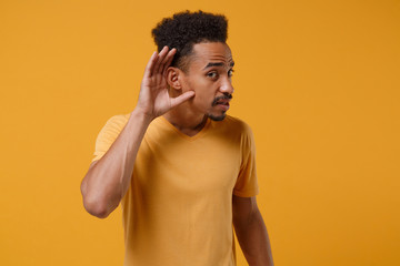 Curious young african american guy in casual t-shirt posing isolated on yellow orange wall...