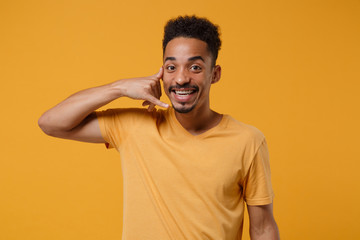 Funny young african american guy in casual t-shirt posing isolated on yellow orange wall background in studio. People lifestyle concept. Mock up copy space. Doing phone gesture like says call me back.