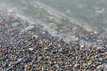 pebble coastline. Seashore with transparent water and small stones.