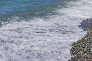 pebble coastline. Seashore with transparent water and small stones.