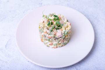 Olivier salad on a white plate, decorated with pea sprouts. Traditional New Year and Christmas Russian salad. Close-up, selective focus.
