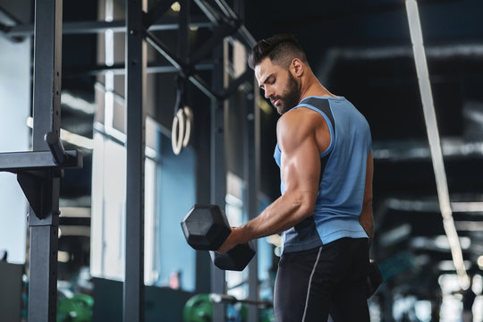 Handsome athlete training arms with dumbbells at gym