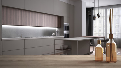 Wooden table top or shelf with aromatic sticks bottles over blurred modern minimalist kitchen with island, stools and accessories, pendant lamps, white architecture interior design