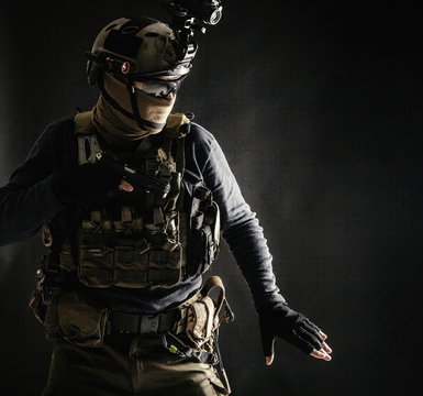 Special operations fighter in helmet with night-vision, thermal imaging device, load carrier carefully moving with caution in darkness, holding hand on pistol, ready for fight during dangerous mission