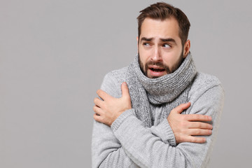 Frozen young man in gray sweater posing isolated on grey wall background, studio portrait. Healthy...