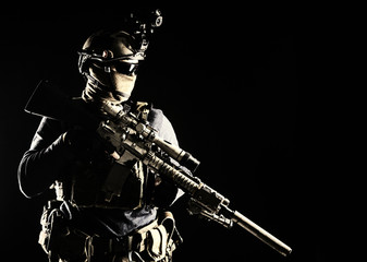 Army elite troops marksman, special operations forces sniper wearing mask and glasses, night-vision or infrared thermal imaging device on helmet, holding service rifle with optical sight and silencer