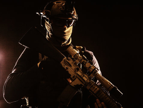 Army elite troops marksman, special operations forces sniper wearing mask and glasses, night-vision or infrared thermal imaging device on helmet, holding service rifle with optical sight and silencer