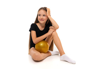 Fototapeta na wymiar young gymnast child in a black sports swimsuit sits with a ball on a white background with copy space