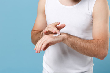 Close up cropped shot of man hand applying moisturizer cream from container isolated on blue pastel background studio portrait. Skin care healthcare cosmetic procedures concept Mock up copy space.